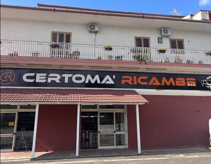 Facciata del negozio con insegna nera «CERTOMA' RICAMBI s.r.l.», tettoia in coppi rossi, ingresso a vetri e balcone bianco